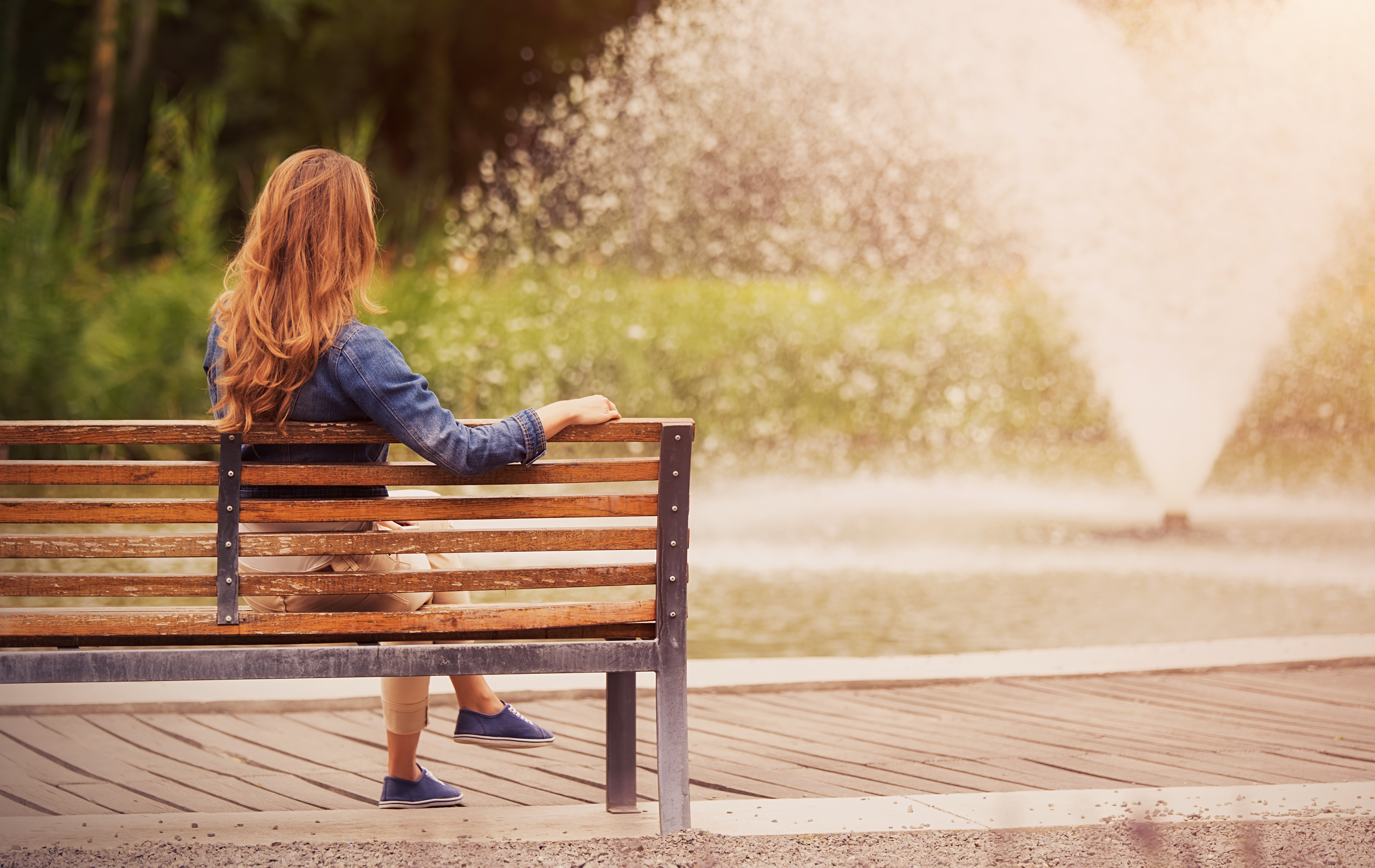 Young woman sitting on bench in park Urban Fountains & Furniture
